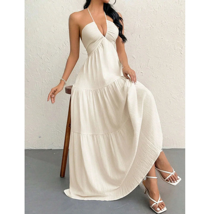 Woman in cream halter maxi dress and white heels sitting on a wooden stool, Rovelli fashion