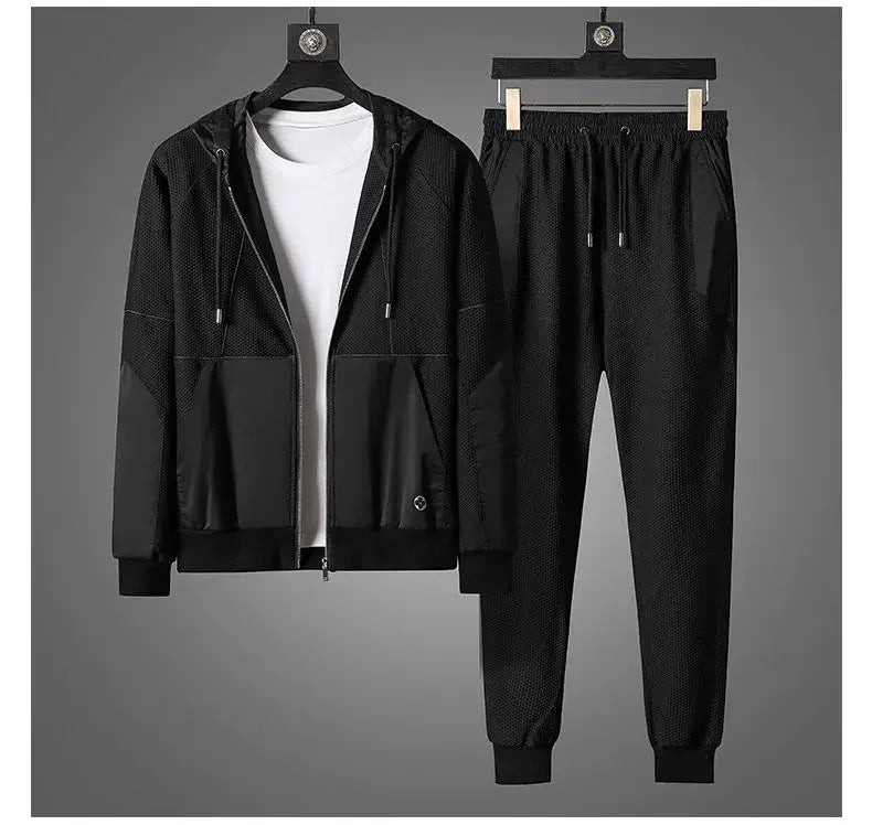 A black activewear set features a zipper hoodie jacket with matching jogger pants, displayed on hangers. A plain white T-shirt is layered underneath, all set against a gray background.
