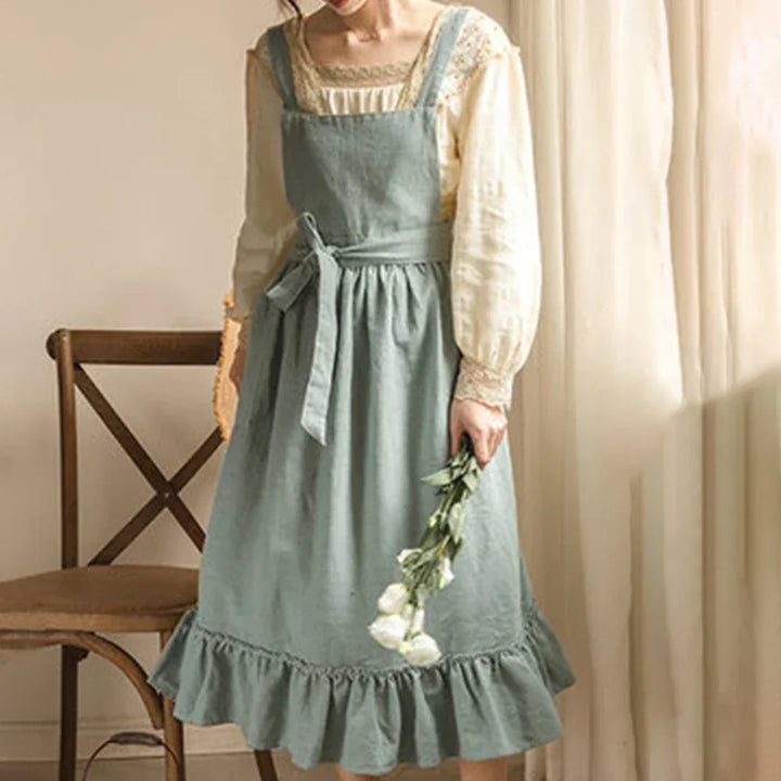 Woman in vintage blue apron dress and cream blouse, holding flowers, Rovelli style