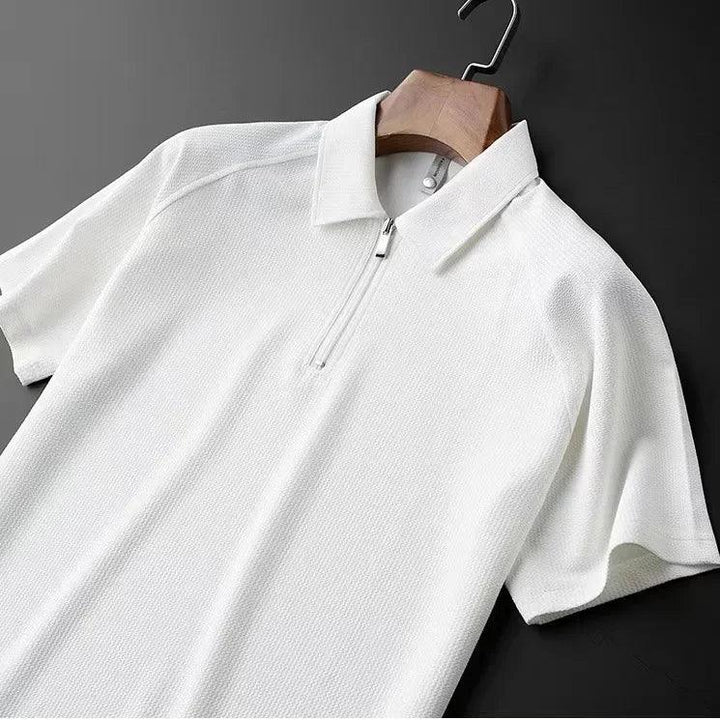 A white short-sleeve mens silk polo with a textured, moisture-wicking fabric, featuring a partial front zipper, displayed on a wooden hanger against a dark background.