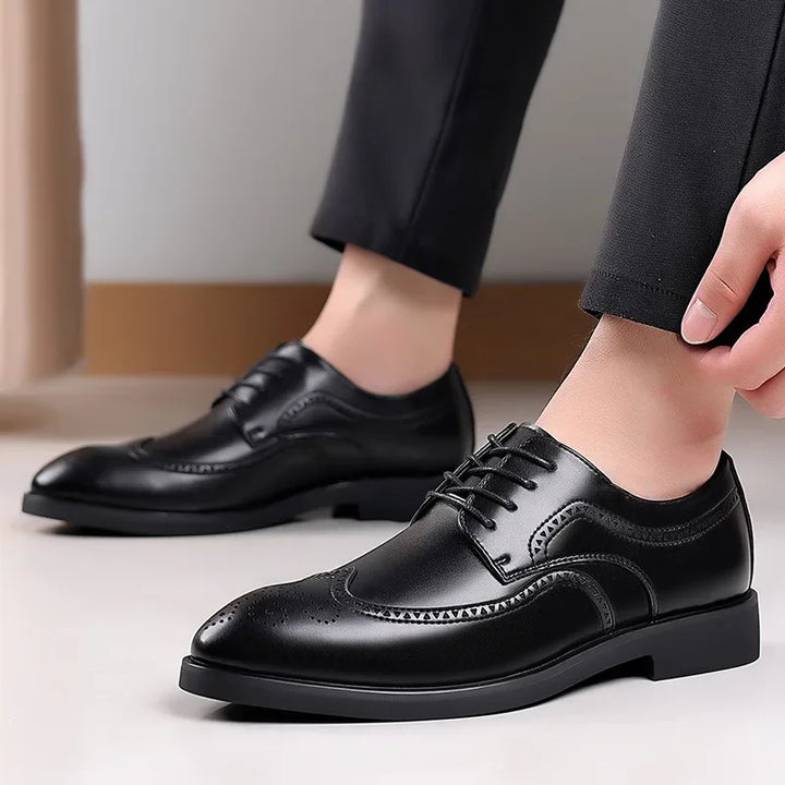 A person wearing black dress pants and premium leather shoes with brogue detailing, adjusting one shoe while standing indoors on a light floor.