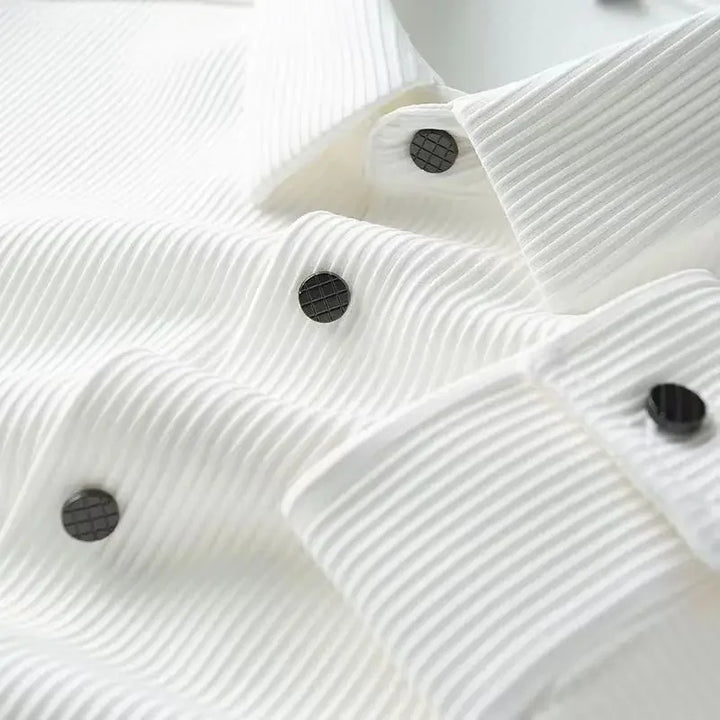 Close-up of a white, ribbed dress shirt crafted from ultra soft fabric with black grid-patterned buttons, showing the textured material and part of the collar and cuffs.