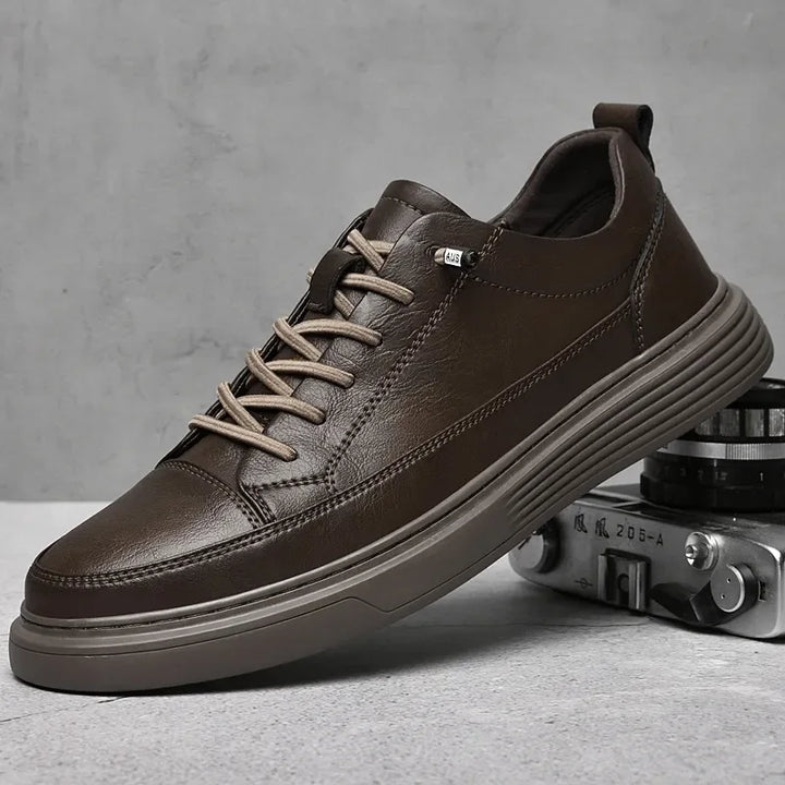 A dark brown genuine leather sneaker with beige laces and a textured rubber sole is displayed against a gray background, with an old-fashioned camera partially visible beside it. Features comfortable RunForm insoles for all-day support.