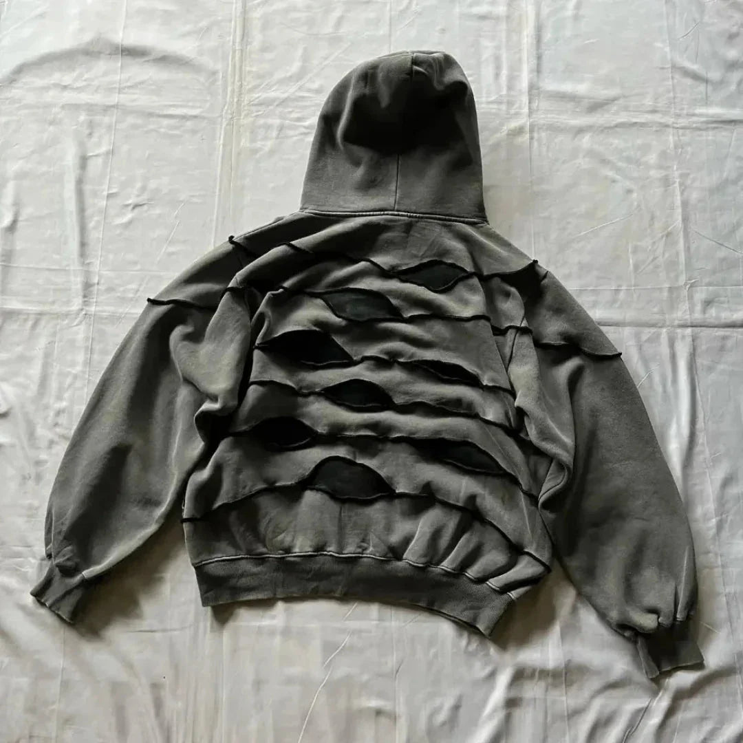 A gray hooded sweatshirt with a comfortable loose fit lies flat on a white surface, featuring multiple horizontal, irregularly shaped cutouts across the back that create a layered, distressed look.