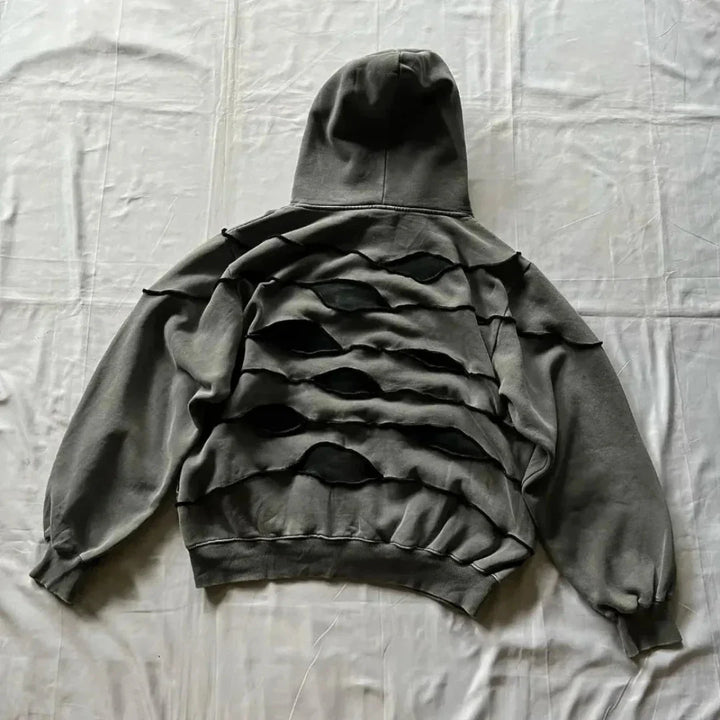 A gray hooded sweatshirt with a comfortable loose fit lies flat on a white surface, featuring multiple horizontal, irregularly shaped cutouts across the back that create a layered, distressed look.
