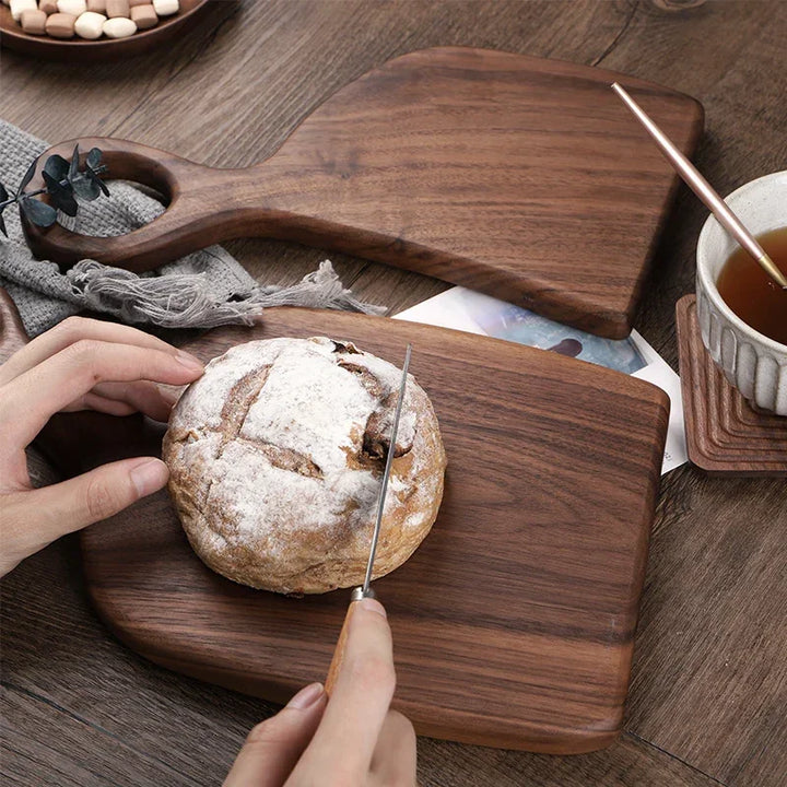 Cutting rustic bread on walnut wood chopping board with tea, kitchen decor by Rovelli