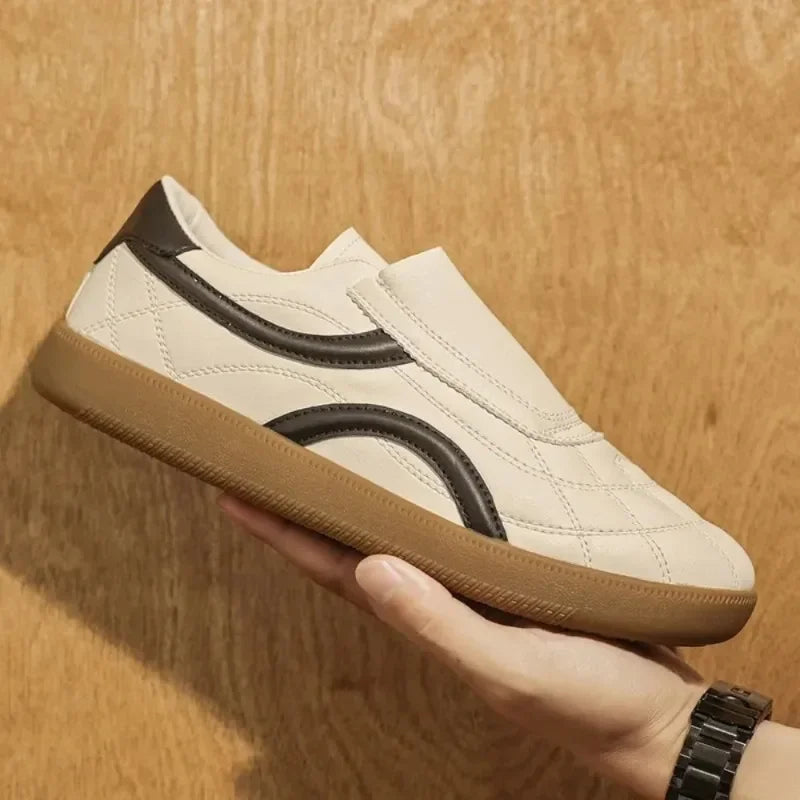Rovelli beige slip-on sneaker with brown sole and black accents, held by hand against wood background