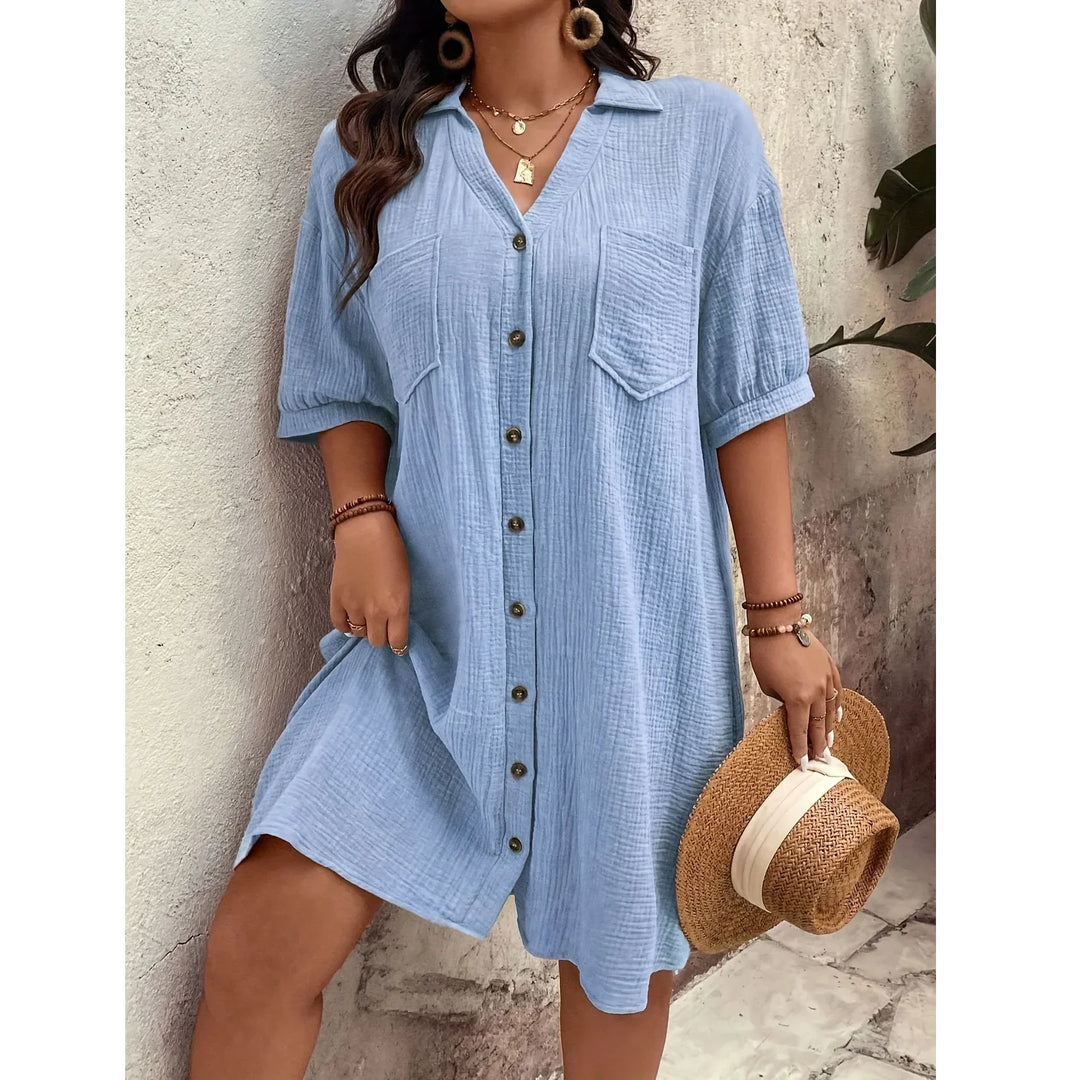 Woman in light blue button-up dress by Rovelli holding straw hat, standing outdoors