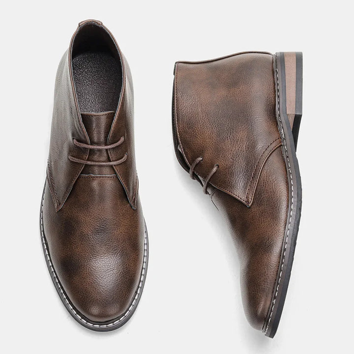 A pair of brown leather boots, Western-inspired chukka style, with round toes and lace-up fronts, shown against a white background—one shoe upright and the other lying on its side.