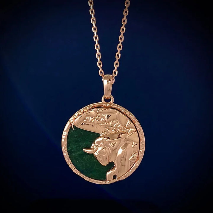 A gold zodiac necklace with a round pendant featuring an embossed bulls head on a green background, displayed against a dark blue backdrop—a striking piece of astrology jewelry.