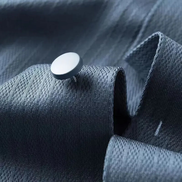 A close-up of a silver pushpin stuck into textured blue-gray fabric, with the material slightly folded around the pin—perfect for showcasing the crisp quality of a spring long-sleeved shirt.