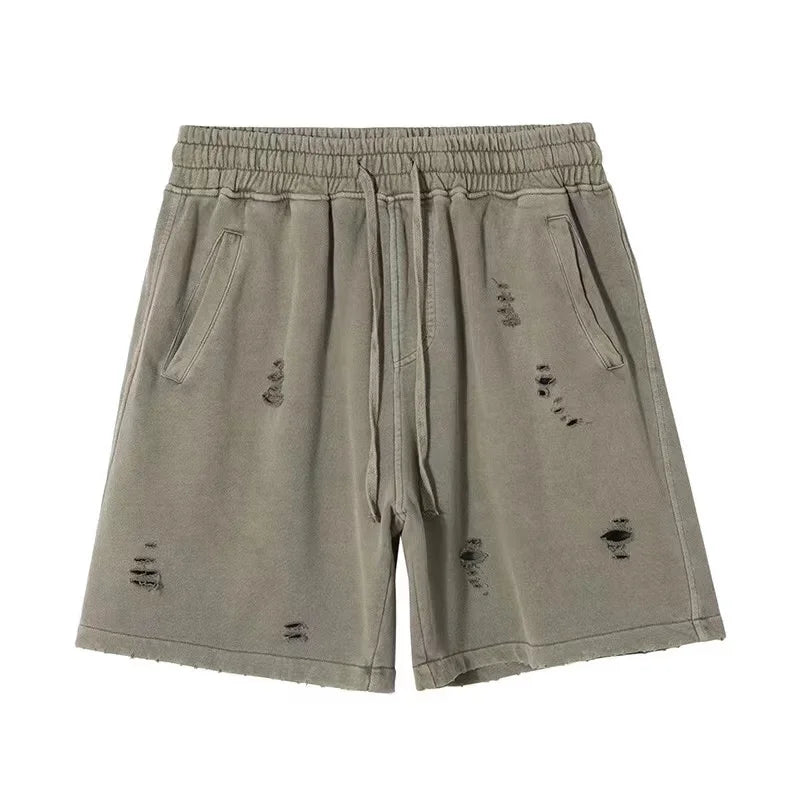 Light olive green vintage baggy shorts with an elastic waistband, drawstring, side pockets, and a cut-up design featuring distressed, ripped details on the front.