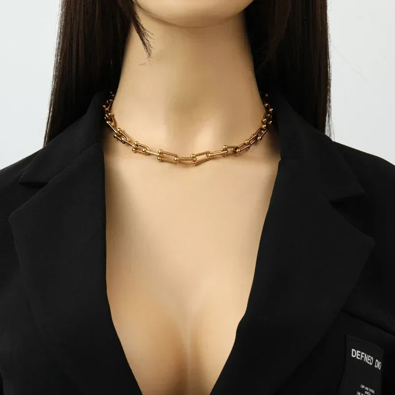 A woman wearing a black blazer and a statement chain necklace with rectangular links in 316L stainless steel, shown from the shoulders to just below the chin.