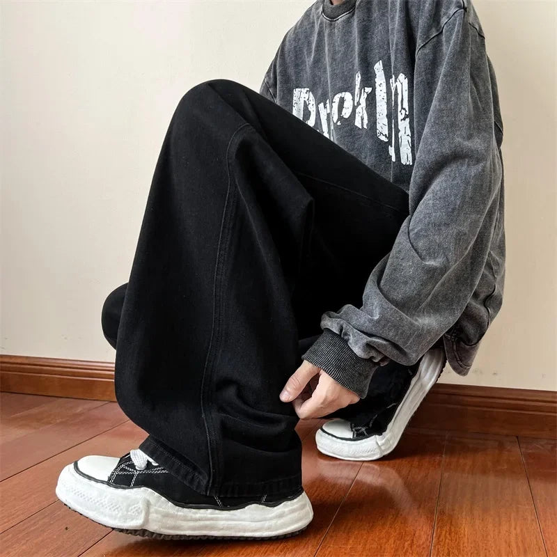A man in premium denim with a relaxed fit sits comfortably on a wood floor, showcasing effortless style and a touch of vintage wash.