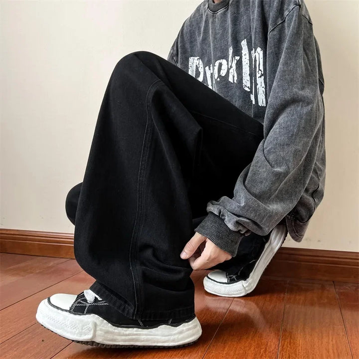 A man in premium denim with a relaxed fit sits comfortably on a wood floor, showcasing effortless style and a touch of vintage wash.