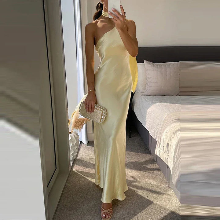Woman in yellow satin one-shoulder dress, pearl clutch, Rovelli fashion bedroom setting