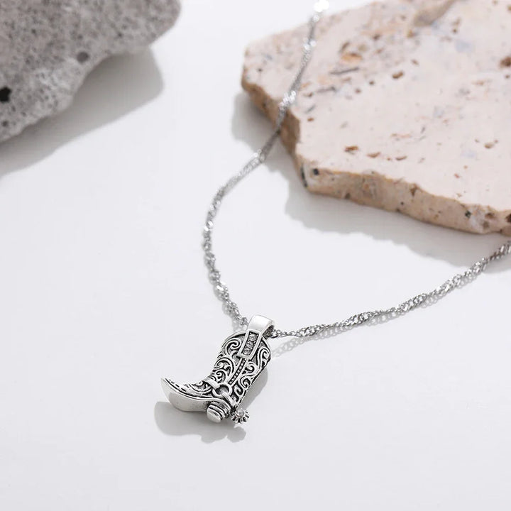 Rovelli silver cowboy boot pendant necklace on chain, styled on neutral stone background