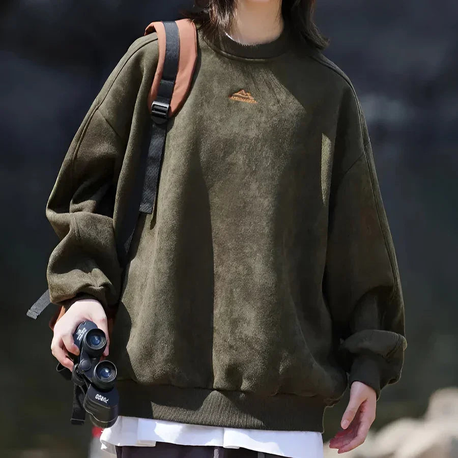 Person in olive green Rovelli sweatshirt outdoors with backpack and binoculars