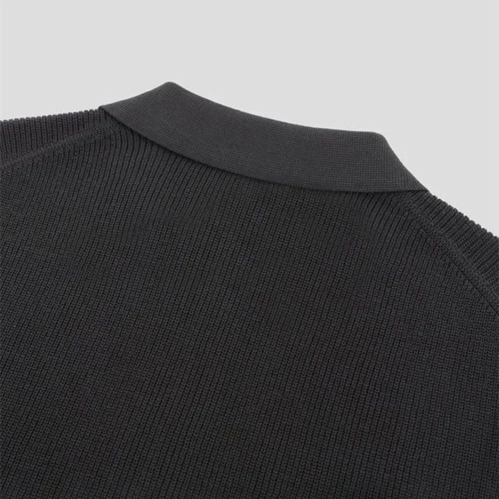 Close-up of the upper back and collar of a black knitted sweater, showing the texture of the fabric and ribbed detailing on the crew neckline against a plain light background.