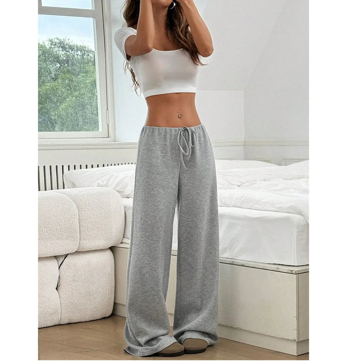 Woman wearing gray wide-leg lounge pants and white crop top in modern bedroom, Rovelli fashion