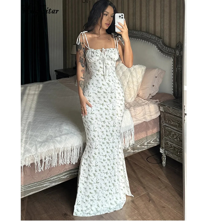 Woman in a long white floral dress taking a mirror selfie in a stylish bedroom, Rovelli fashion