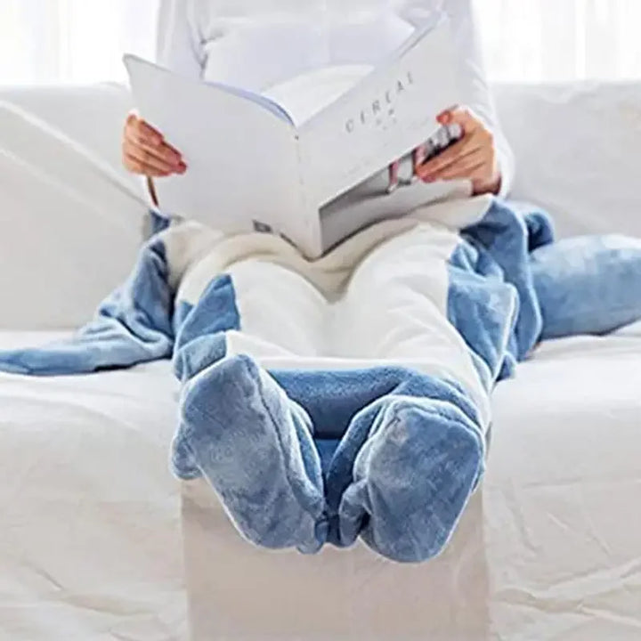 A person sits on a white couch, wrapped in cozy pajamas with foot pockets, reading a magazine or book.