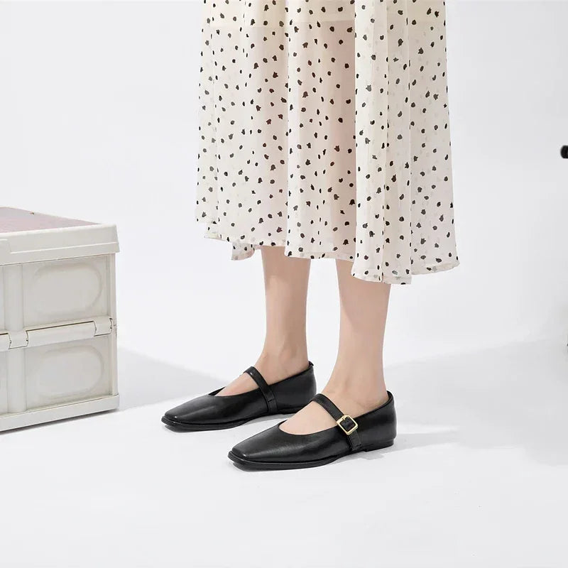 A person wearing a white midi skirt with black polka dots and stylish sheepskin ladies shoes with gold buckles stands on a white floor next to a white storage box.