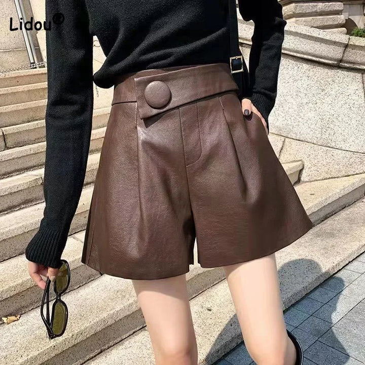 A person wearing high-waisted calfskin leather shorts with button detail and a black long-sleeve top stands outside on stone steps, holding sunglasses in one hand.