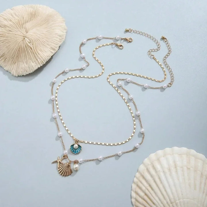Gold layered sea shell charm necklace with pearls, displayed on light blue with seashells, Rovelli