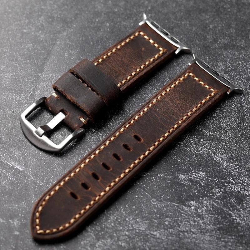 Two pieces of a handcrafted dark brown Italian cowhide leather watch strap, saddle stitched with beige thread and finished with silver metal hardware, are displayed on a textured dark surface.