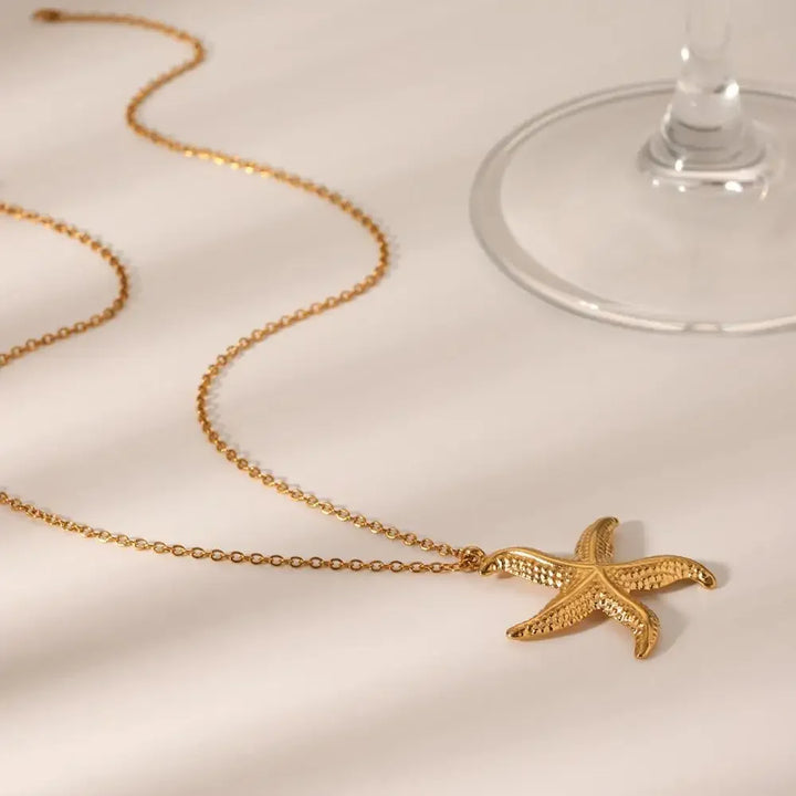 Gold starfish pendant necklace by Rovelli on light surface near a wine glass
