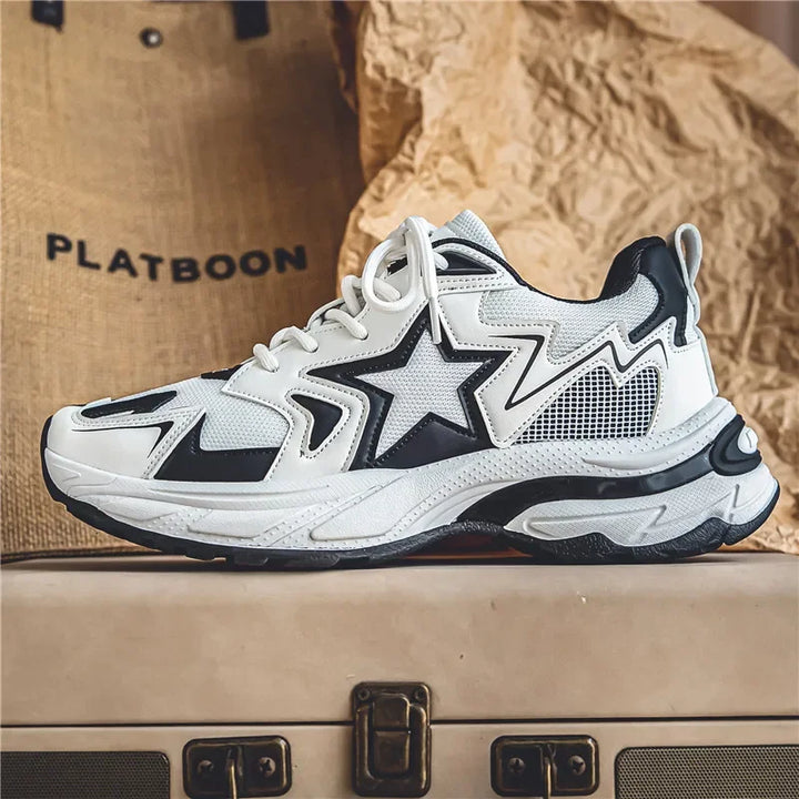 A stylish white sneaker with black accents, a star design on the side, and chunky sole features a durable rubber outsole. Displayed on a suitcase with a beige textured background, the word PLATBOON is partially visible.