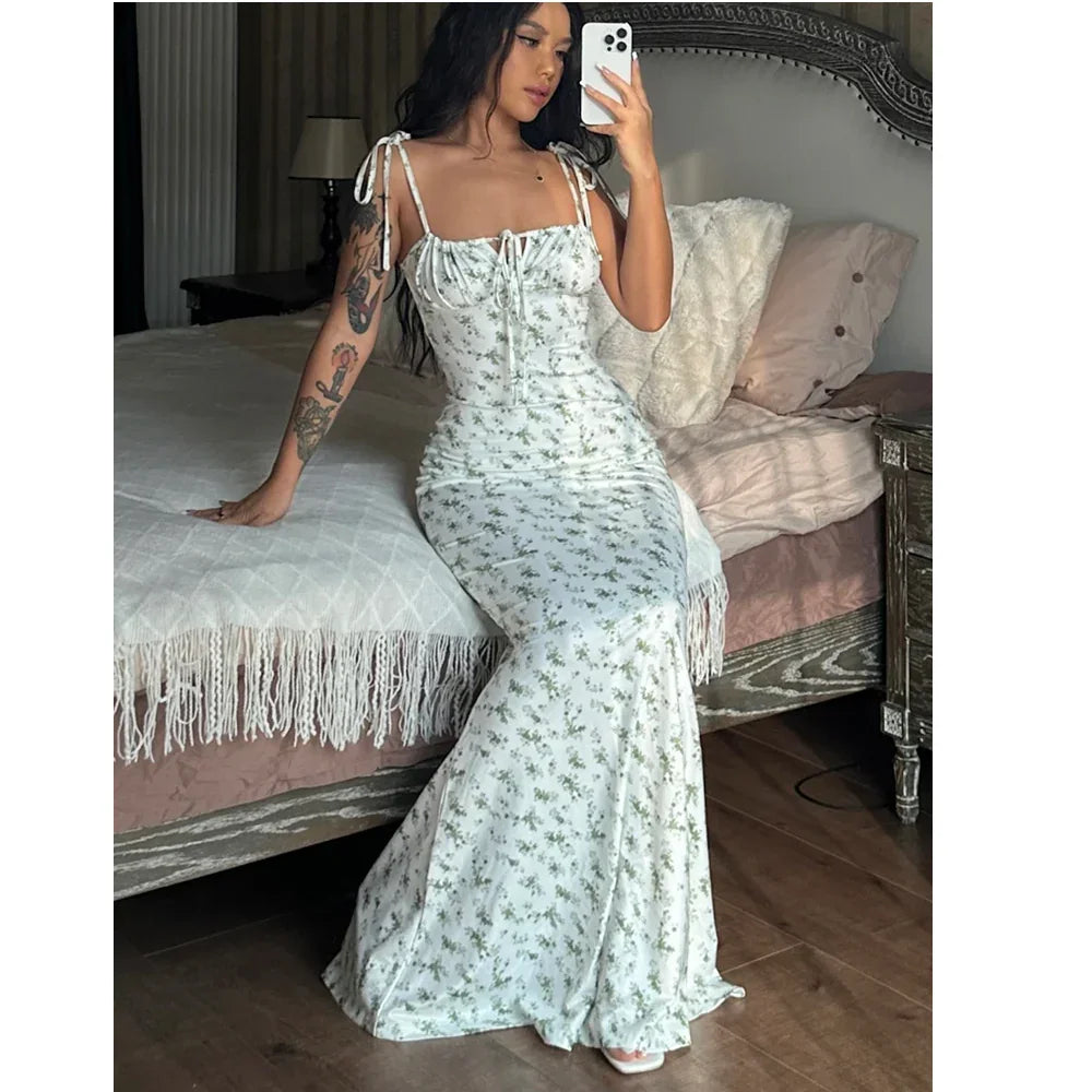 Woman in floral maxi dress taking mirror selfie on elegant bed, Rovelli fashion style