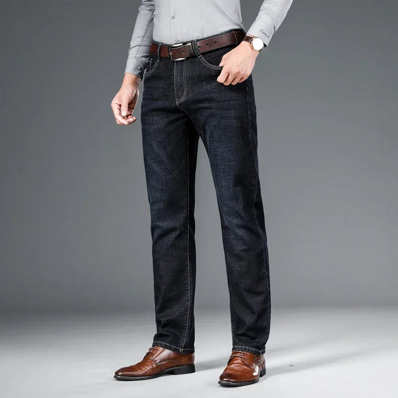 Man wearing dark blue jeans, brown belt, dress shoes, and grey shirt, Rovelli fashion.