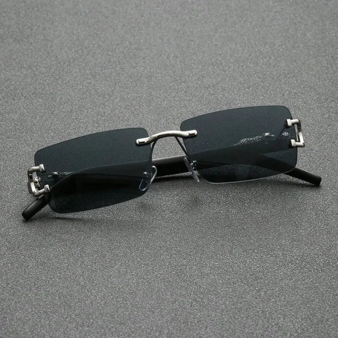 A pair of rectangular, rimless black sunglasses with durable hinges, metal bridge and temples, resting on a textured gray surface.