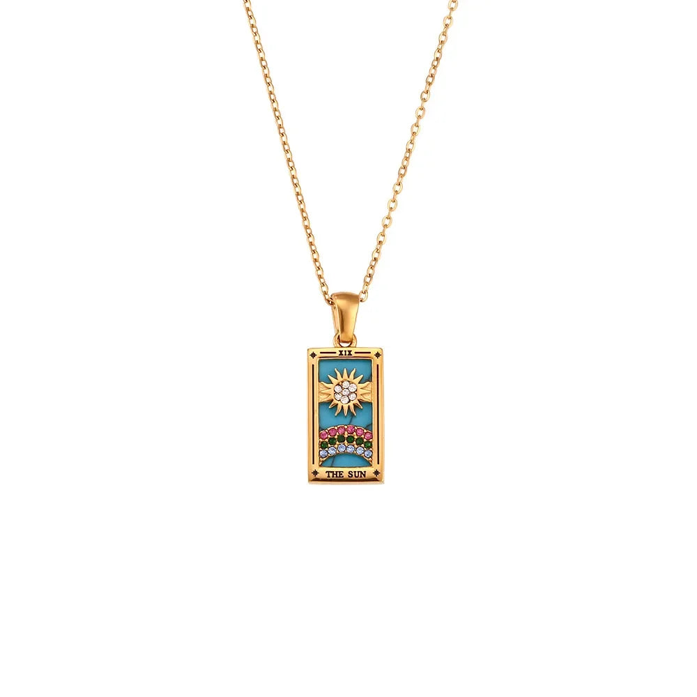 The Solaris Pendant Necklace features a rectangular 18K gold-plated chain with a colorful, tarot-inspired design. The pendant, accented with blue enamel, depicts a sun above a landscape and bears the words The Sun at the bottom.