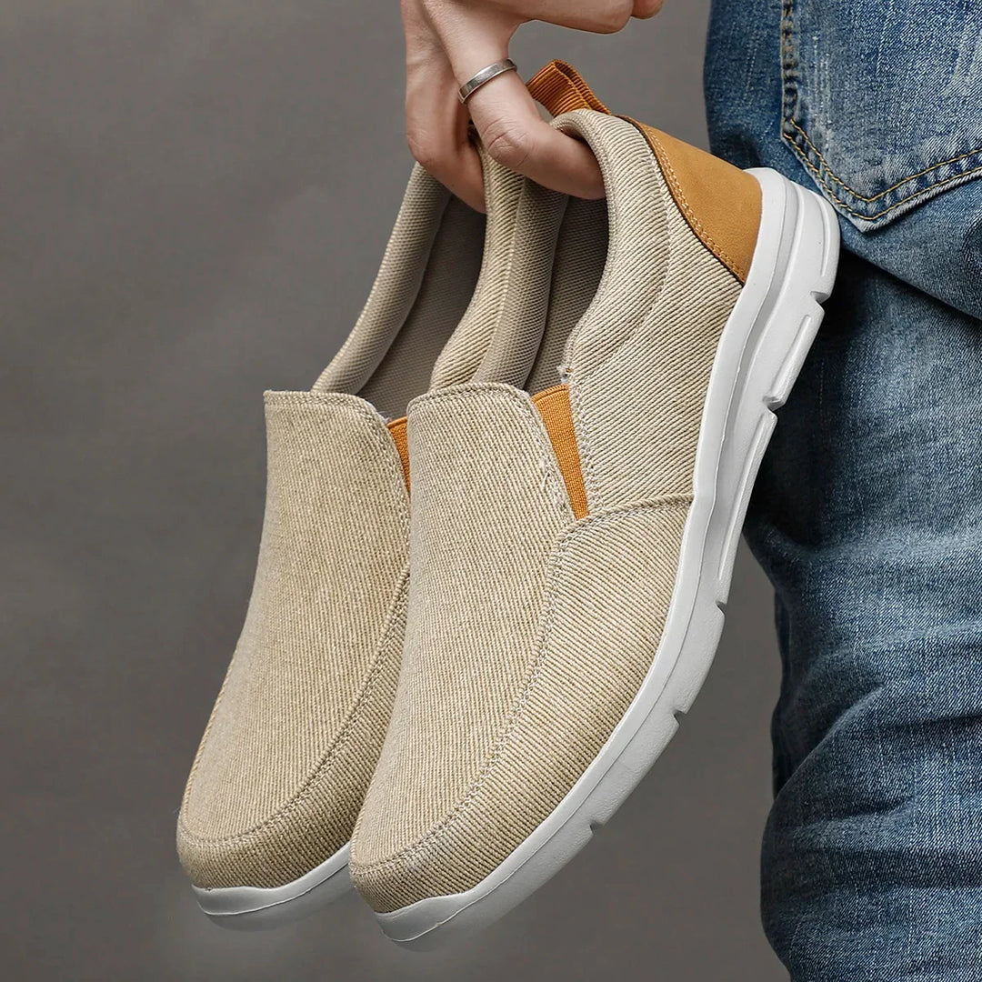 Rovelli beige slip-on canvas shoes with white sole, held by hand next to jeans