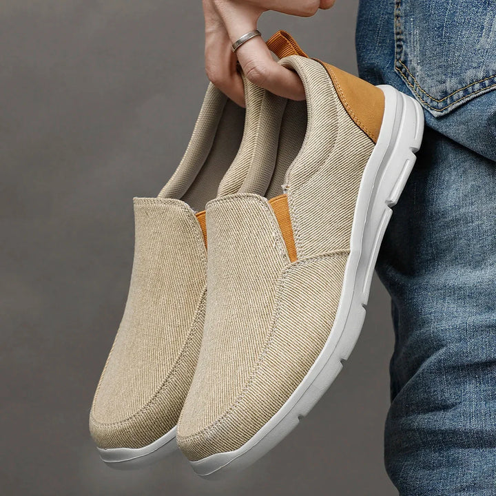 Rovelli beige slip-on canvas shoes with white sole, held by hand next to jeans