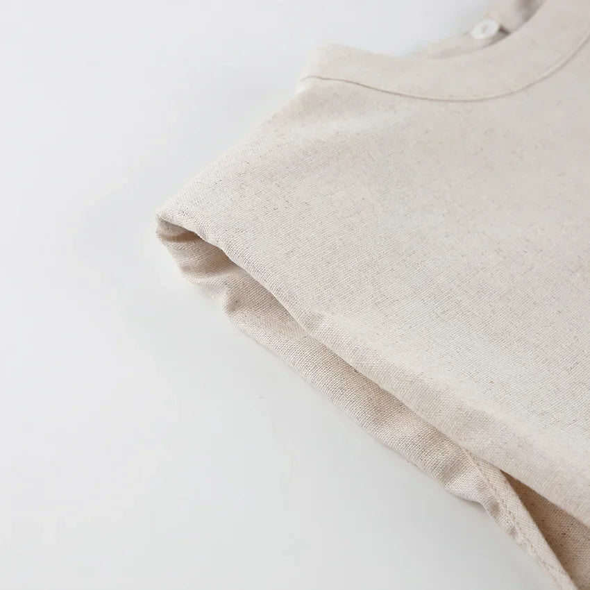 A close-up of a beige, short-sleeve shirt made of textured Belgian Linen Blend fabric, neatly laid on a white surface with one sleeve folded inward.