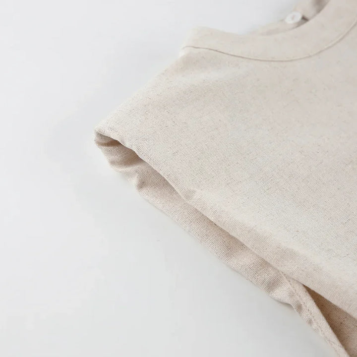 A close-up of a beige, short-sleeve shirt made of textured Belgian Linen Blend fabric, neatly laid on a white surface with one sleeve folded inward.