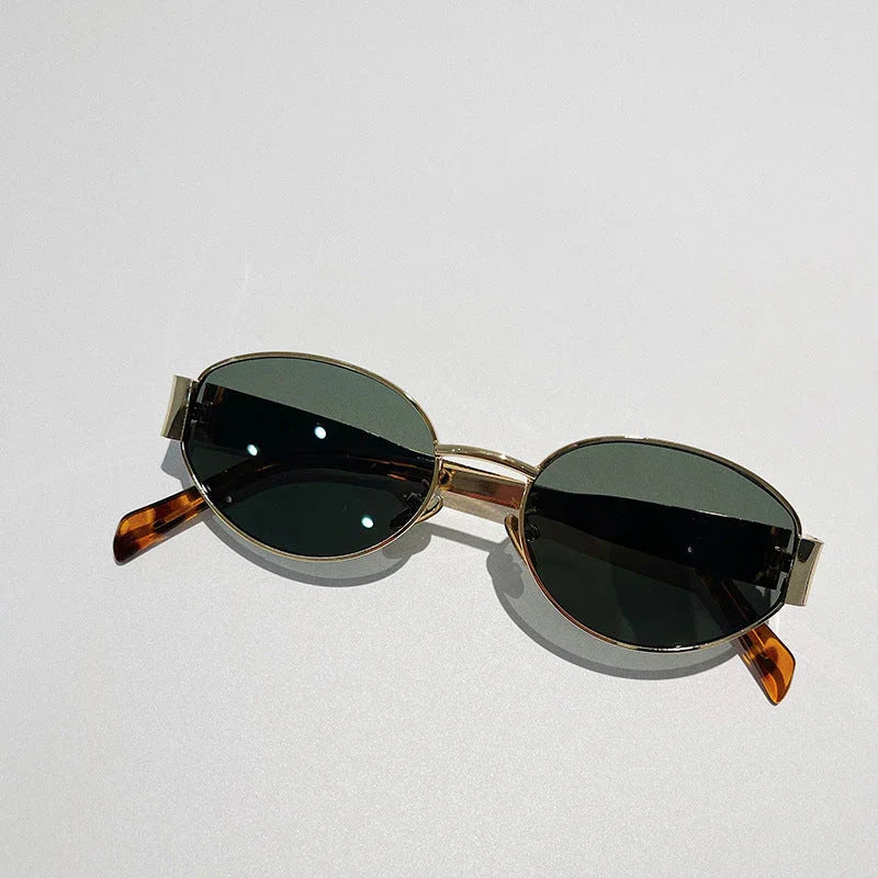 A pair of vintage-inspired, oval-shaped sunglasses with dark UV400 protection lenses, gold metal frames, and brown tortoiseshell arms, placed on a light-colored surface.
