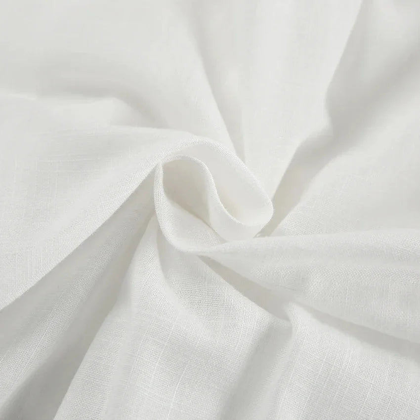Close-up of soft, white fabric with a subtle texture, gently gathered and twisted in the center—perfect for a chic romper, adding natural folds and smooth flow ideal for a stylish summer outing.
