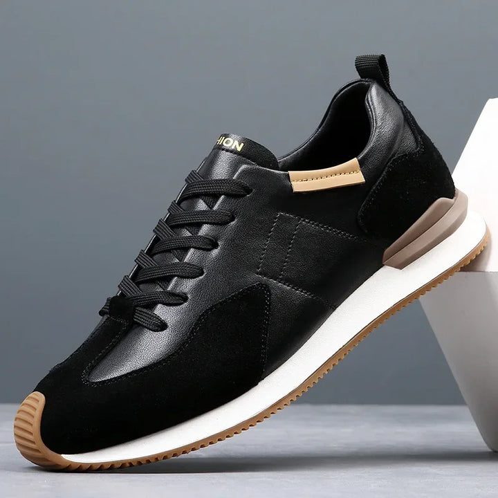 A black athletic sneaker with black laces, a white sole, tan accents on the heel and collar, and a brown rubber outsole provides excellent arch support, displayed against a gray background.