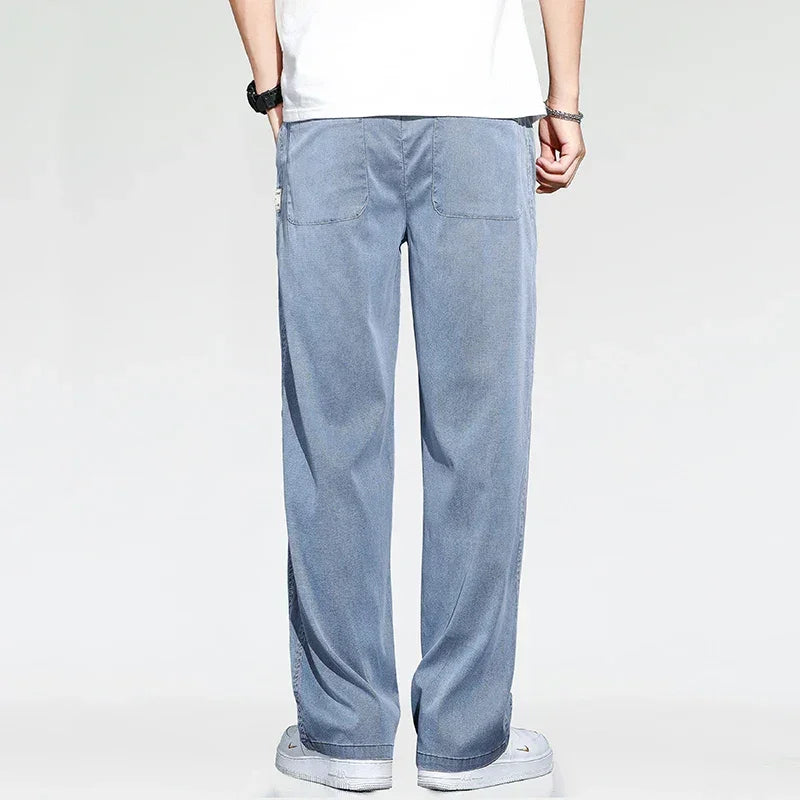 A person wearing summer loose men jeans, a white T-shirt, white sneakers, and a wristwatch is standing with their back to the camera against a plain light background.