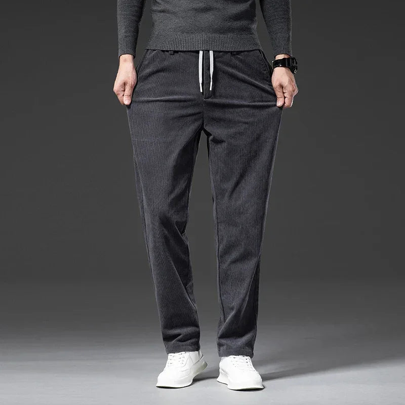 A person wearing dark gray men's smart casual pants with a drawstring, a matching long-sleeve shirt, and white sneakers stands against a plain dark background. Their hands are in their pockets.