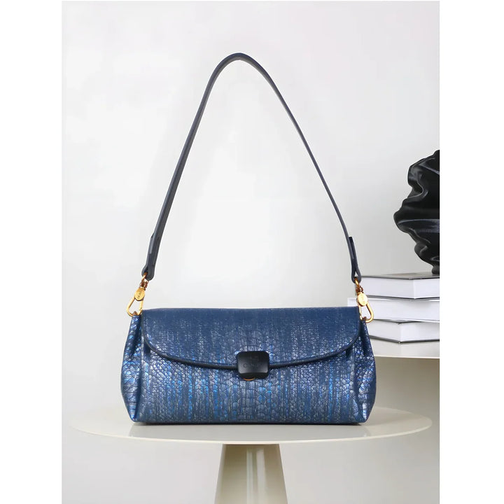 Rovelli blue textured shoulder bag with gold hardware on a round table, books in background