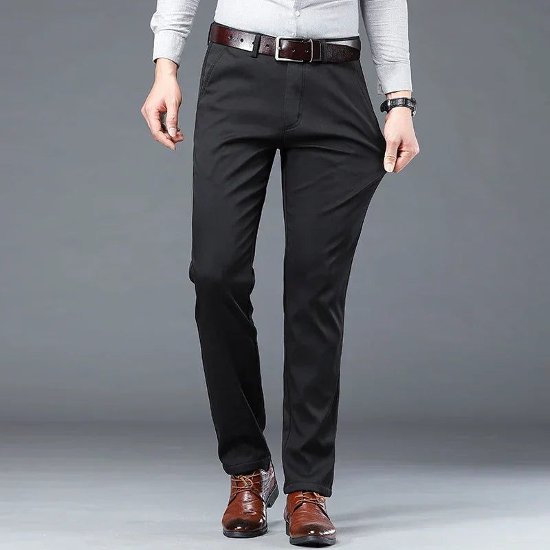 A person wearing a light gray long-sleeve shirt, black dress pants with a tailored fit, a brown belt, and brown dress shoes stands against a plain gray background. Their hands are resting at their sides.