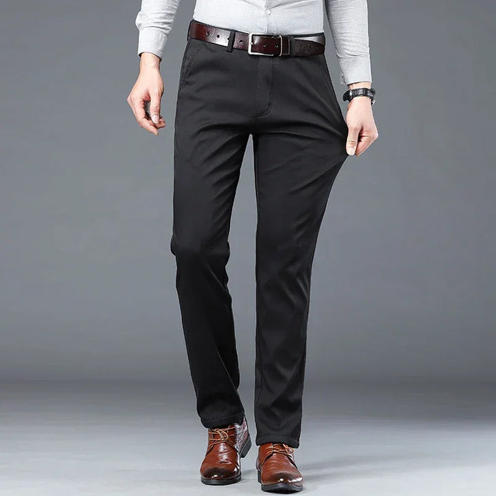 A person wearing a light gray long-sleeve shirt, black dress pants with a tailored fit, a brown belt, and brown dress shoes stands against a plain gray background. Their hands are resting at their sides.