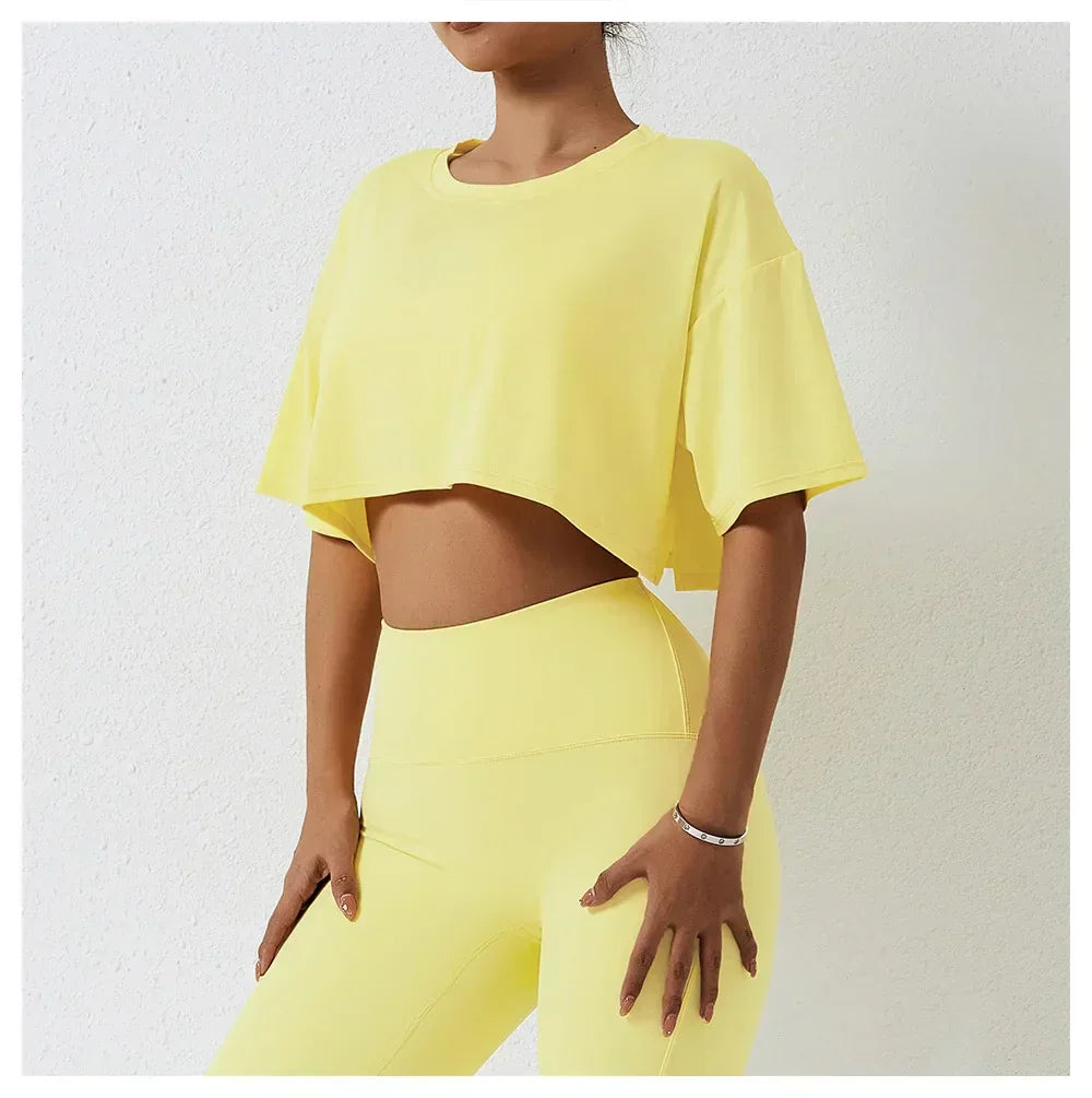 Woman wearing a relaxed fit, cotton crop top and matching high-waisted yellow leggings, standing against a light-colored wall with her hands resting on her thighs.