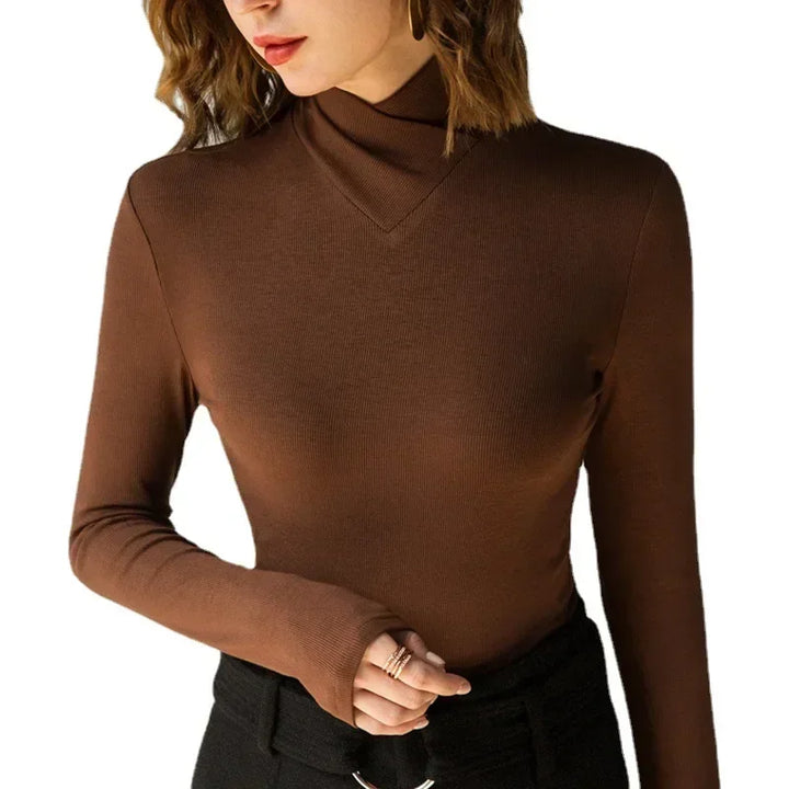 A woman wearing a fitted brown stand-up collar T-shirt and black pants stands against a white background, with her left hand partially tucked into her sleeve and her head turned slightly to the side—an effortless fall/winter essential look.
